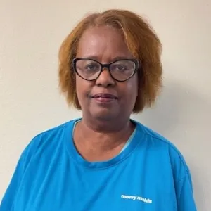 smiling woman with a blue merry maids uniform standing in front of a tan wall